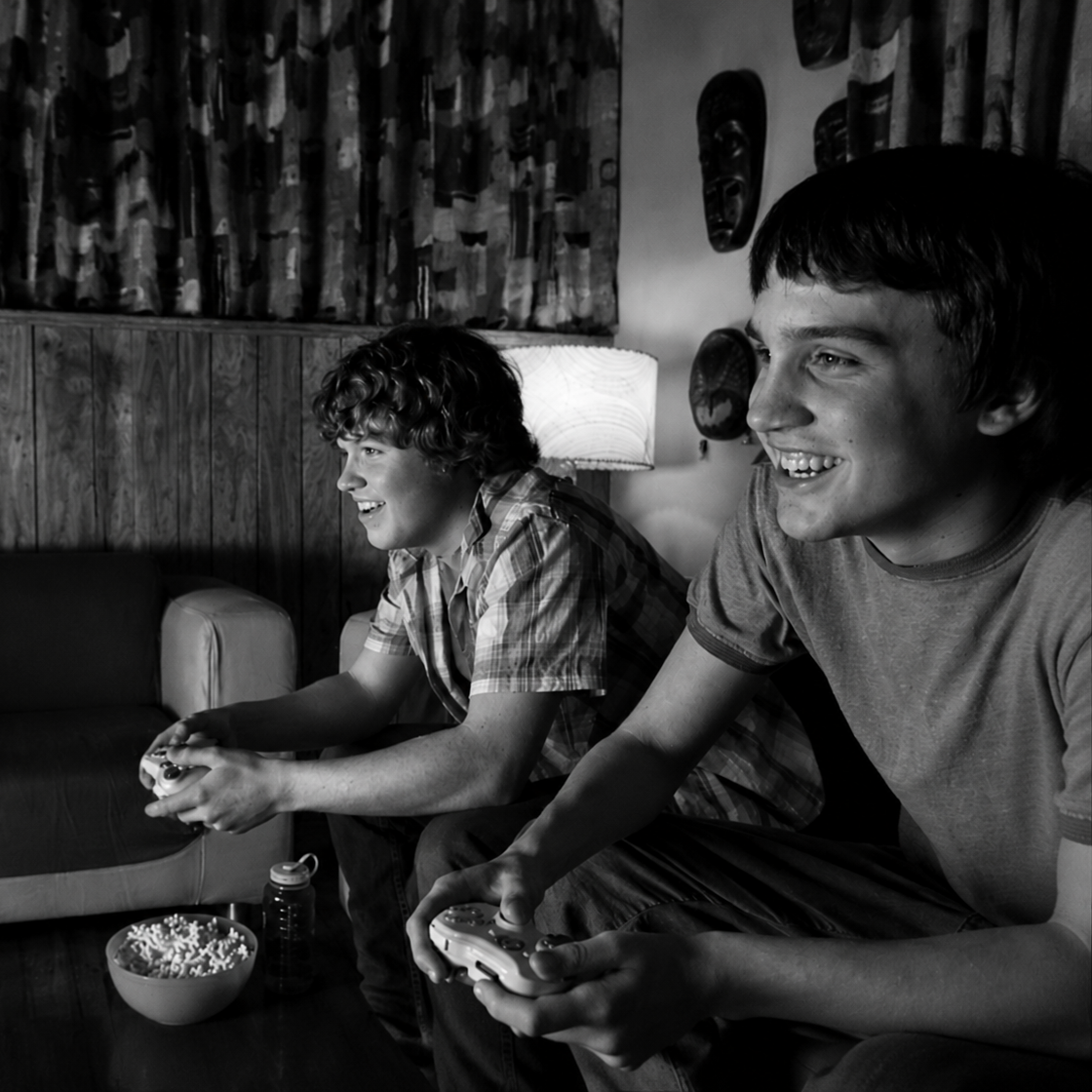 Black-and-white Our Story image showing two friends playing video games with controllers in a living room, representing shared retro gaming memories.