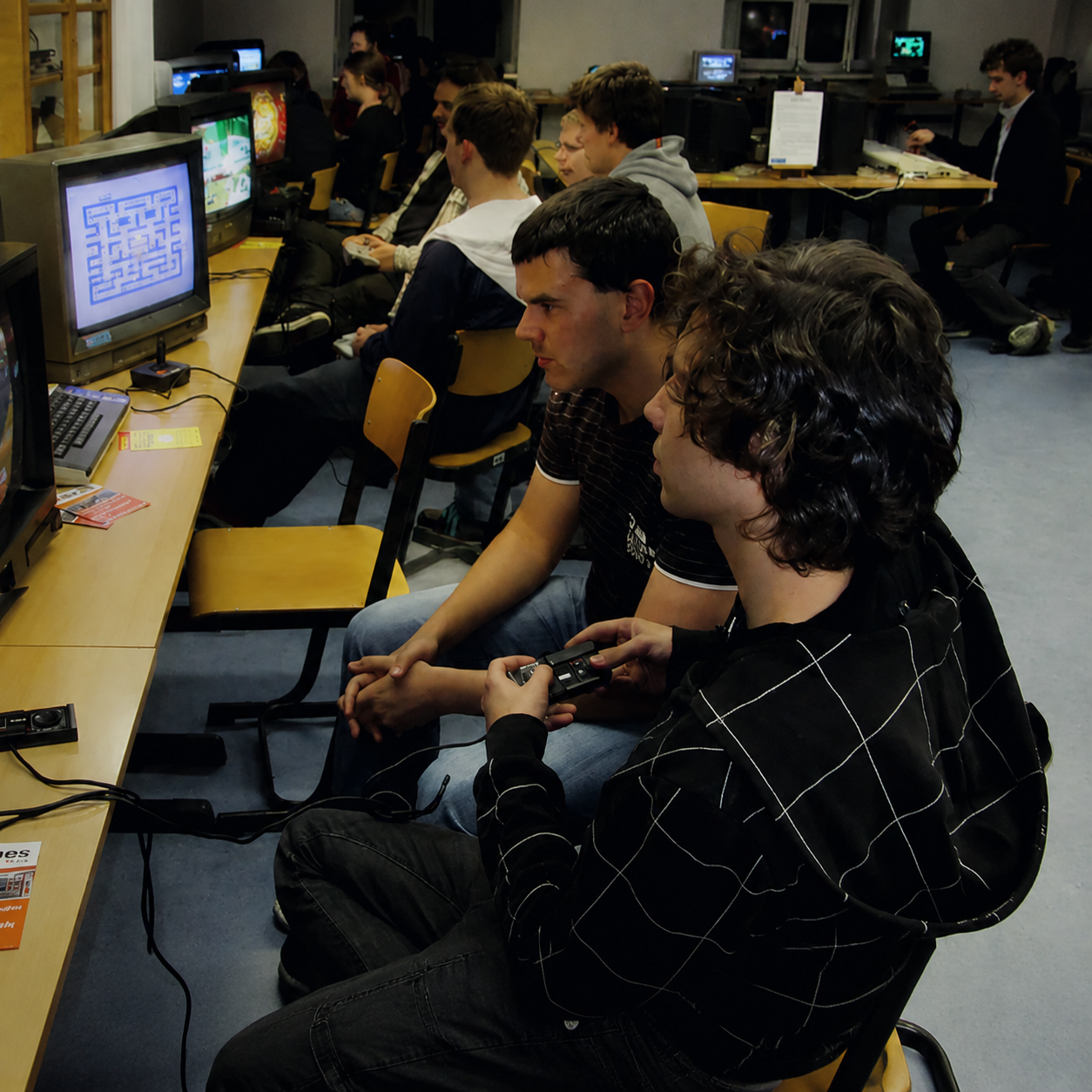 Our Story image showing retro gaming players in a community room using controllers and CRT televisions during a classic game session.